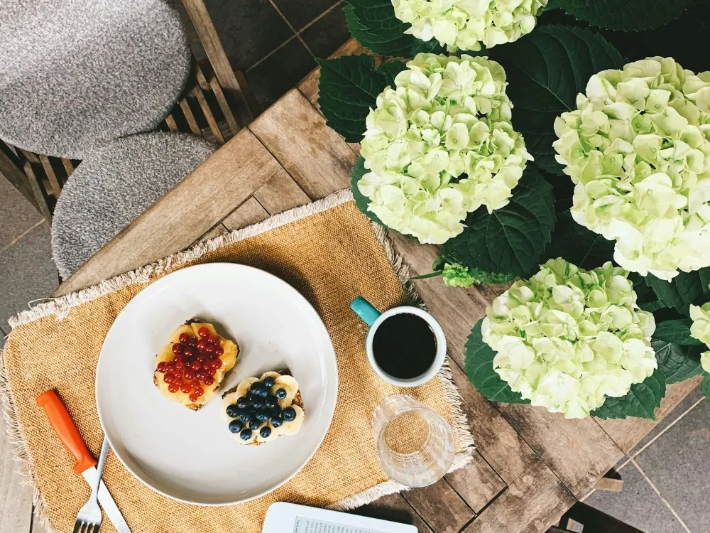 Un petit-déjeuner sur une table de terrasse en bois, près d’hortensias blancs